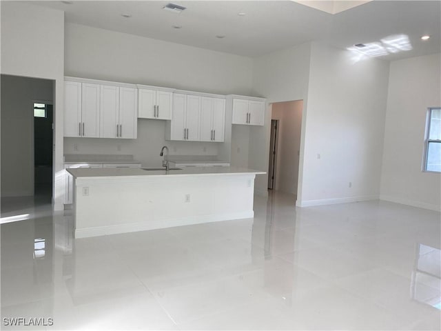 kitchen with a towering ceiling, a center island with sink, white cabinets, and a sink