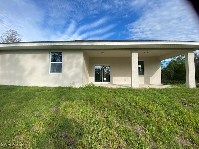 rear view of house featuring a yard and stucco siding