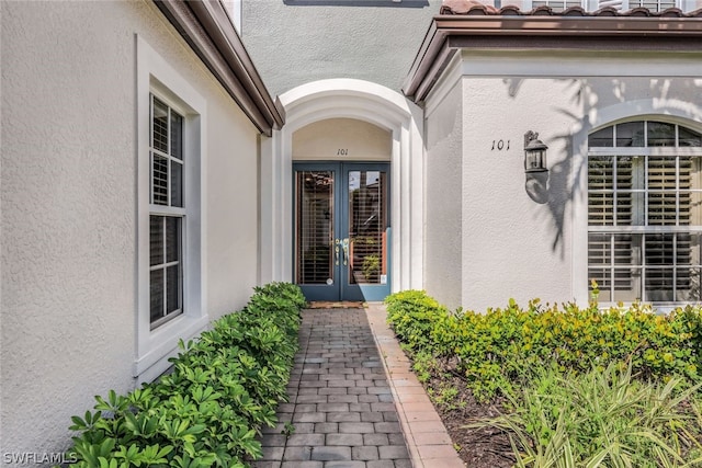 view of exterior entry with a tiled roof, french doors, and stucco siding