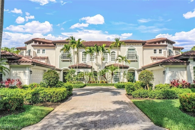 mediterranean / spanish house with a garage, driveway, a tiled roof, and stucco siding