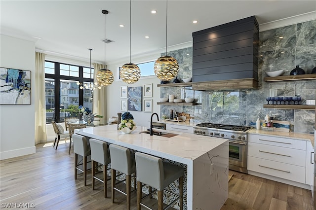 kitchen featuring range with two ovens, a center island with sink, ornamental molding, white cabinets, and sink