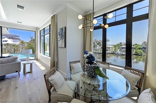 dining area featuring a notable chandelier, crown molding, hardwood / wood-style flooring, and a water view