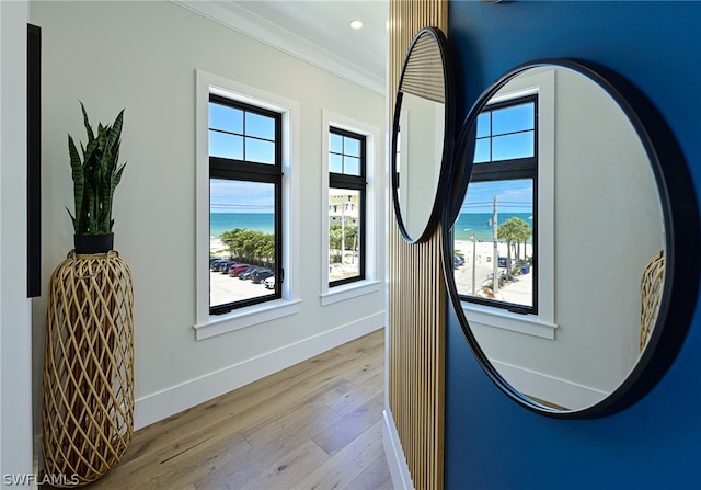 hallway with ornamental molding, light hardwood / wood-style flooring, and a water view