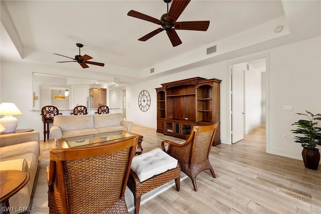 living room featuring light hardwood / wood-style flooring, a raised ceiling, and ceiling fan