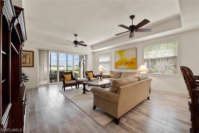 living room featuring a raised ceiling, light hardwood / wood-style flooring, and ceiling fan