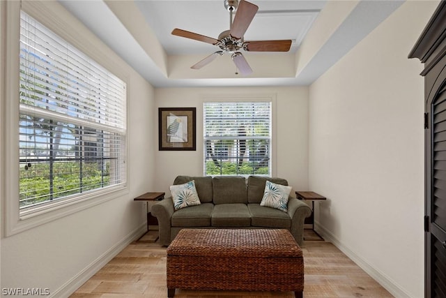 living room with light hardwood / wood-style flooring, a raised ceiling, and ceiling fan