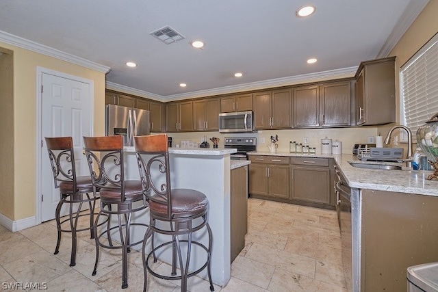 kitchen with a kitchen island, appliances with stainless steel finishes, sink, ornamental molding, and light stone countertops