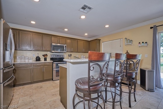 kitchen featuring a breakfast bar area, crown molding, a center island, appliances with stainless steel finishes, and light stone countertops