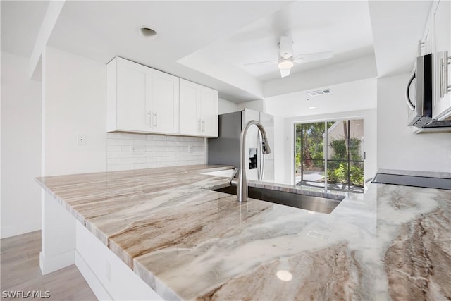 kitchen with light stone countertops, white cabinetry, kitchen peninsula, and sink