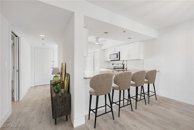 kitchen featuring appliances with stainless steel finishes, a breakfast bar, white cabinets, decorative backsplash, and light hardwood / wood-style flooring