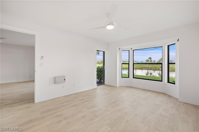 empty room featuring light wood-type flooring, ceiling fan, a healthy amount of sunlight, and a water view