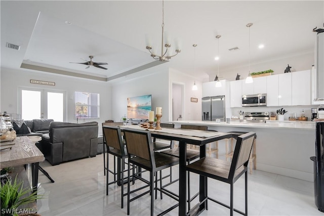 kitchen with white cabinets, ceiling fan with notable chandelier, hanging light fixtures, appliances with stainless steel finishes, and a tray ceiling