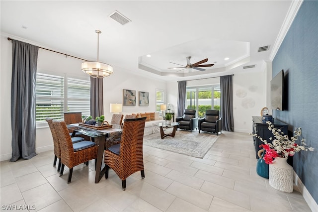 tiled dining area with ceiling fan with notable chandelier, a tray ceiling, and crown molding