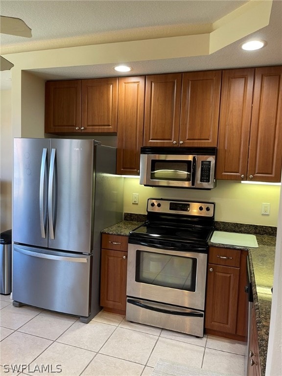 kitchen featuring light tile patterned floors, appliances with stainless steel finishes, and dark stone counters