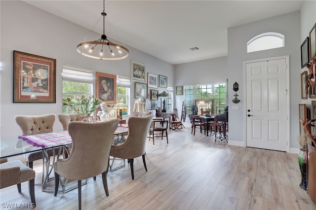 dining room featuring a chandelier, a towering ceiling, and light hardwood / wood-style floors