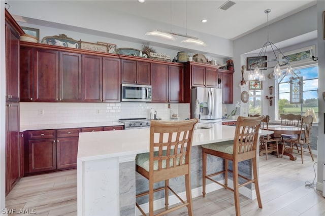 kitchen with hanging light fixtures, backsplash, appliances with stainless steel finishes, a kitchen island, and light wood-type flooring