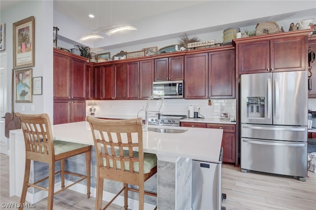 kitchen with appliances with stainless steel finishes, backsplash, sink, a center island with sink, and light hardwood / wood-style floors