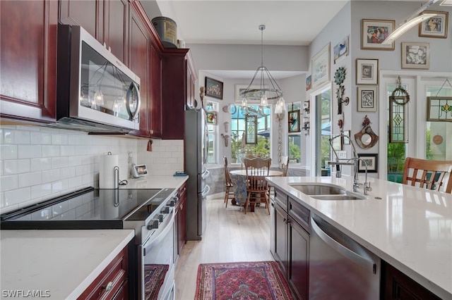 kitchen featuring sink, decorative backsplash, light wood-type flooring, decorative light fixtures, and stainless steel appliances