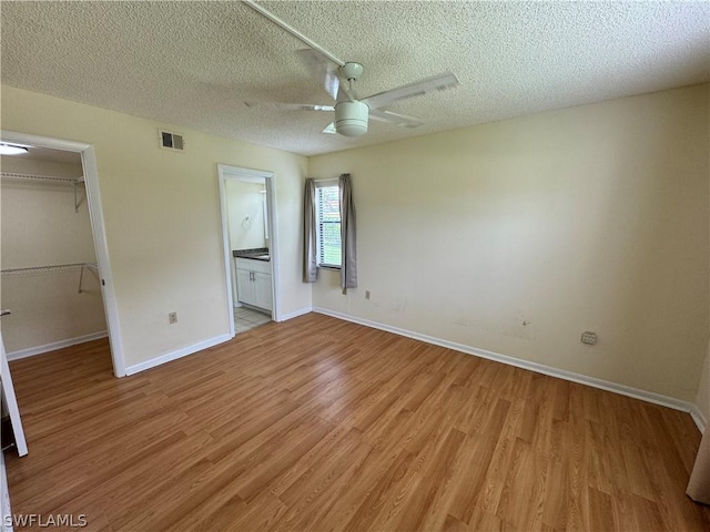 unfurnished bedroom featuring ceiling fan, light hardwood / wood-style flooring, ensuite bathroom, a walk in closet, and a closet