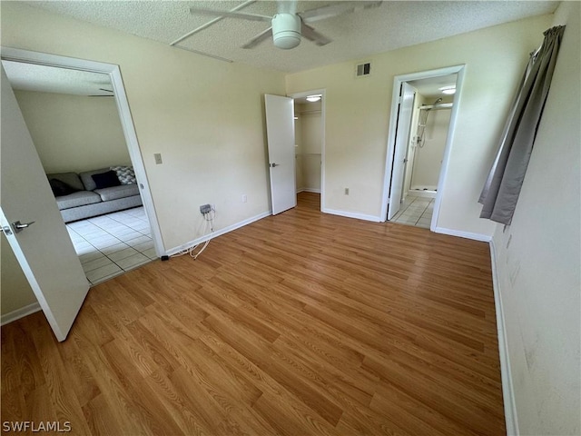 unfurnished bedroom with ensuite bath, ceiling fan, light hardwood / wood-style floors, a walk in closet, and a closet