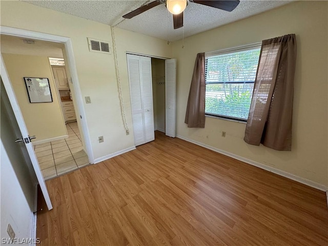 unfurnished bedroom featuring a textured ceiling, light wood-type flooring, a closet, and ceiling fan