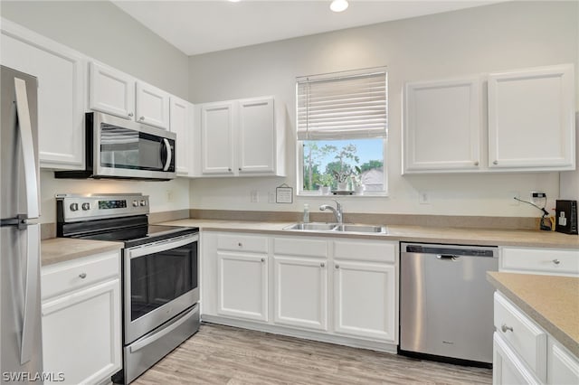 kitchen with white cabinets, appliances with stainless steel finishes, light countertops, light wood-style floors, and a sink