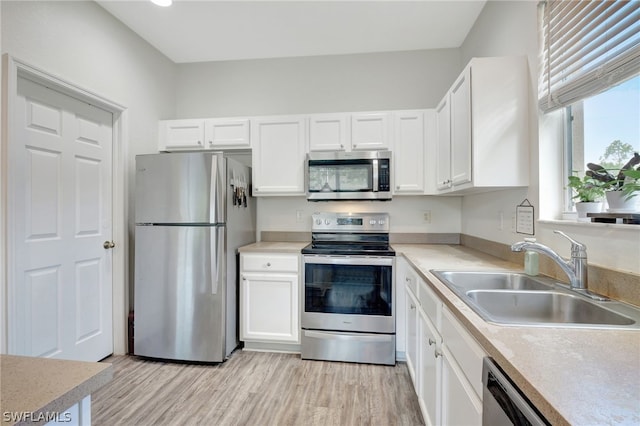 kitchen with stainless steel appliances, sink, white cabinetry, and light hardwood / wood-style floors