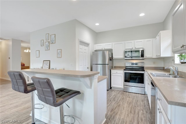 kitchen with light wood finished floors, appliances with stainless steel finishes, a kitchen breakfast bar, light countertops, and a sink