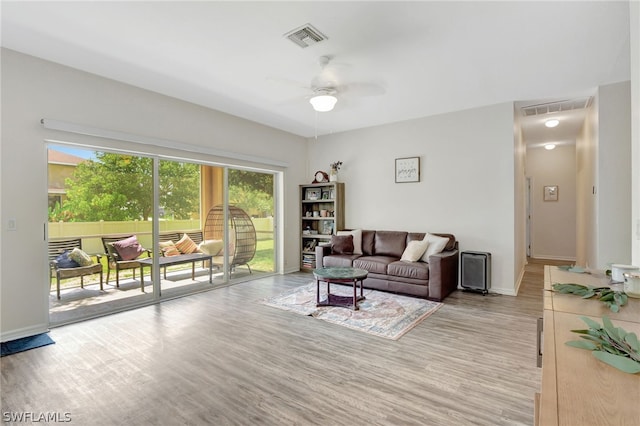 living area featuring baseboards, visible vents, ceiling fan, and light wood finished floors