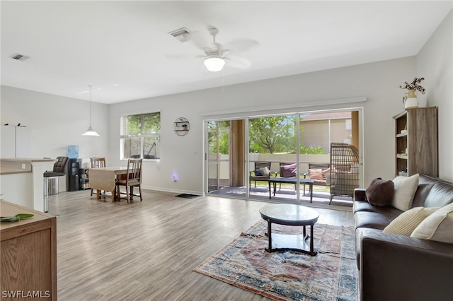 living room with baseboards, visible vents, ceiling fan, and light wood finished floors