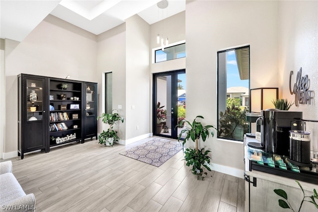 foyer entrance featuring french doors, a towering ceiling, baseboards, and wood finished floors