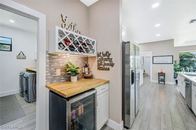 bar with beverage cooler, appliances with stainless steel finishes, independent washer and dryer, decorative backsplash, and a bar