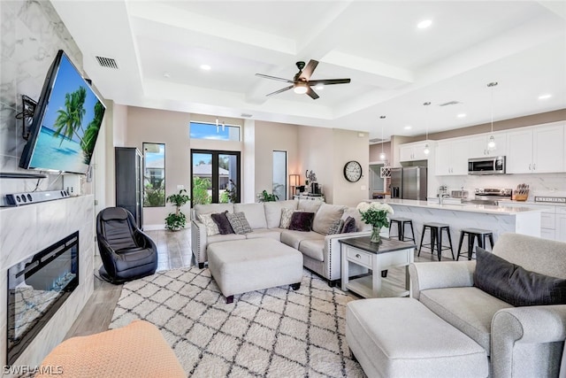 living room with beam ceiling, visible vents, light wood-style flooring, a high end fireplace, and coffered ceiling