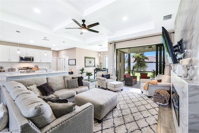 living room with visible vents, light wood-style flooring, a ceiling fan, coffered ceiling, and beamed ceiling