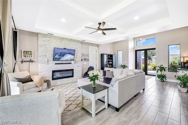 living room with beam ceiling, coffered ceiling, a premium fireplace, light hardwood / wood-style flooring, and ceiling fan with notable chandelier