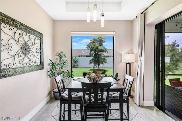 dining area with light wood-type flooring, baseboards, and a raised ceiling