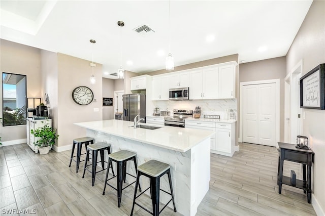 kitchen with visible vents, decorative backsplash, appliances with stainless steel finishes, a kitchen breakfast bar, and a sink