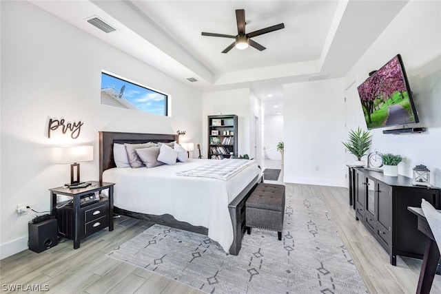 bedroom with baseboards, light wood-style flooring, visible vents, and a tray ceiling