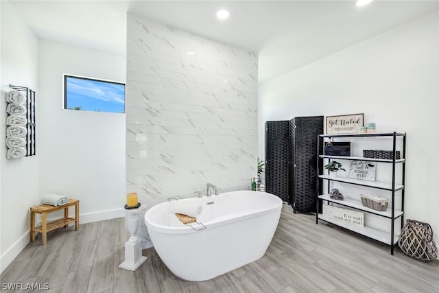 bathroom featuring a soaking tub, baseboards, wood finished floors, and recessed lighting