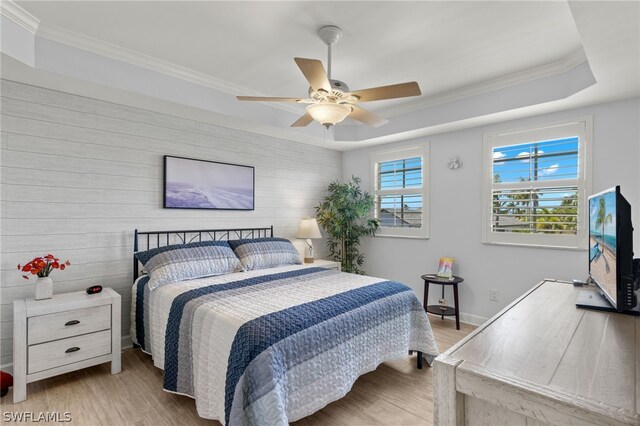 bedroom featuring ceiling fan, light hardwood / wood-style flooring, crown molding, a tray ceiling, and wooden walls