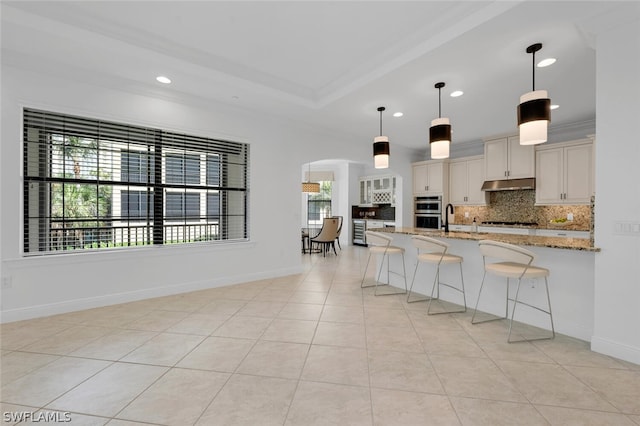 kitchen featuring backsplash, pendant lighting, light stone countertops, stainless steel appliances, and light tile patterned floors