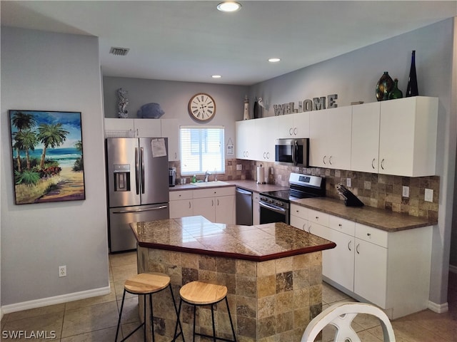 kitchen with appliances with stainless steel finishes, backsplash, sink, light tile flooring, and a kitchen bar