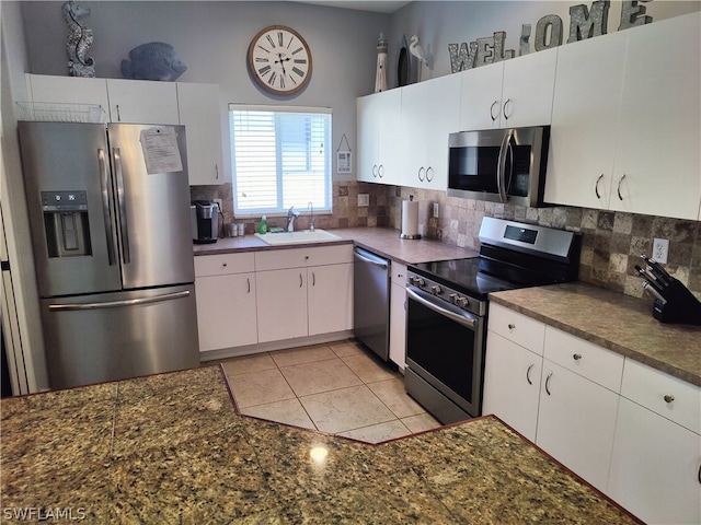 kitchen with appliances with stainless steel finishes, white cabinets, sink, tasteful backsplash, and light tile floors