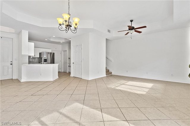 unfurnished living room featuring ceiling fan with notable chandelier, a tray ceiling, and light tile floors