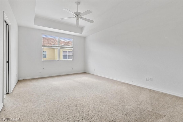 carpeted spare room featuring a raised ceiling and ceiling fan