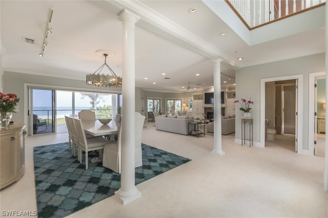 dining space with a notable chandelier, light colored carpet, track lighting, a water view, and ornamental molding