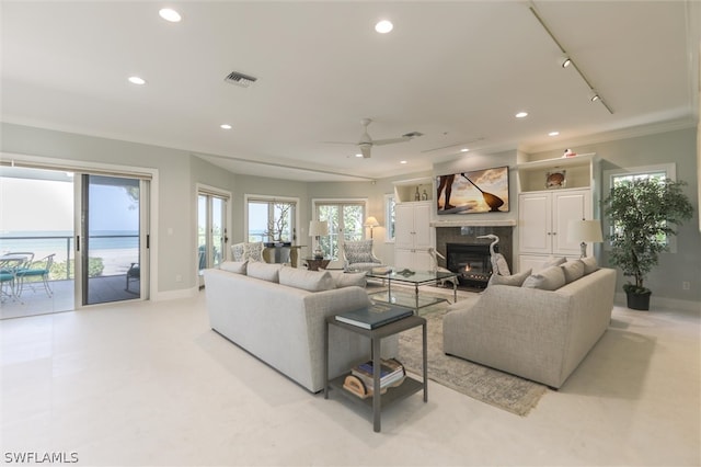 living room featuring a high end fireplace, ceiling fan, a water view, and ornamental molding