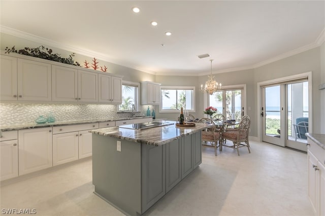 kitchen featuring decorative backsplash, crown molding, stone countertops, white cabinets, and a kitchen island