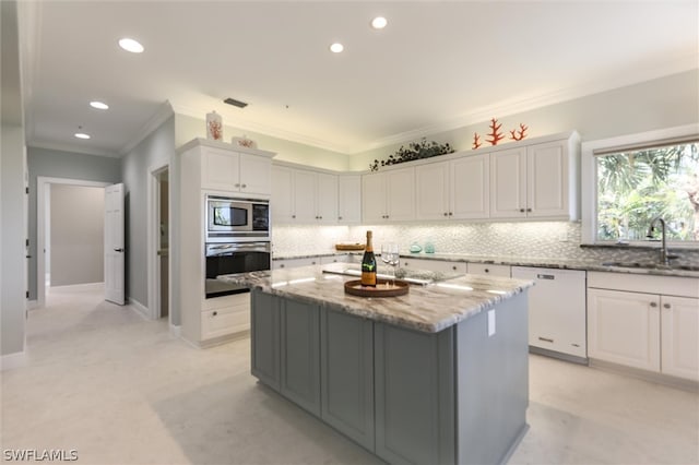 kitchen with white cabinets, crown molding, appliances with stainless steel finishes, a kitchen island, and light stone counters