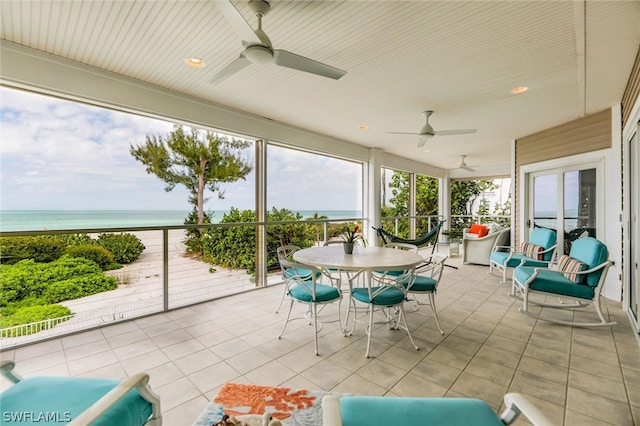 sunroom featuring ceiling fan, a water view, and a view of the beach